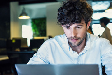 Serious young businessman using laptop in office