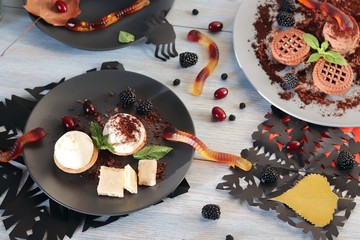 Halloween food, autumn leaves and dessert with chocolate, ice cream and jelly worms on a wooden...