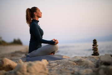 Fototapeta na wymiar Zen-like woman practicing Yoga on a rock at the beach.