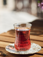 Tea in a glass of armudu on a saucer, located on a wooden table in the loggia. In the background are flowers . Bright sunny day. Close-up.
