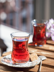 Two glasses of armudu tea on a saucer, located on a wooden table in the loggia. A piece of cane sugar and a spoon on a saucer. Bouquet of wildflowers in ukgu table. Bright sunny day. Close-up.