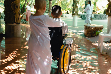 The little nun pushes the wheelchair of a disabled boy,Morning sun light,Natural background in religious buildings,Lifestyle of special child in education age of children,Happy disability kid concept.