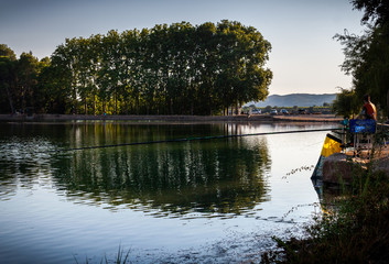 Obraz premium Fishermen fishing with fishing rod on the shore of the lake on a sunny afternoon
