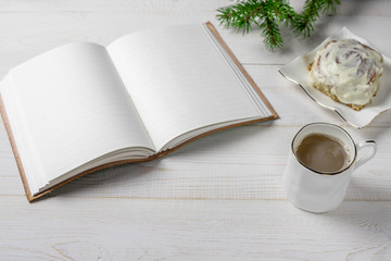 Cinnamon rolls or cinnabon for Christmas. Homemade traditional winter festive dessert buns pastry on white background, with a Christmas tree branch, a cup of coffee and a notebook