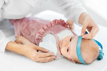 Obraz na płótnie Canvas medicine, healthcare and pediatrics concept - female pediatrician doctor with measure tape measuring baby girl patient's head at clinic or hospital