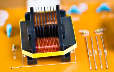 Magnetic ferrite core transformer detail on beige printed circuit board. Close-up of induction...