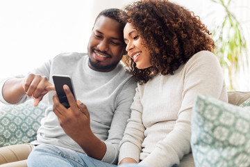 technology, internet and people concept - happy african american couple with smartphone at home