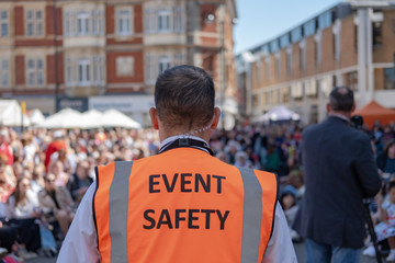 Shallow focus of an Event Safety officer seen facing members of the public in a town square. The...