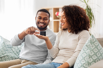 internet of things and technology concept - happy african american couple with smart speaker sitting on sofa at home