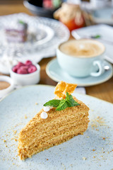 Honey sponge cake decorated with meringue and mint leaves.. Breakfast in the cafe, morning coffee. Cappuccino and lots of desserts on the table.