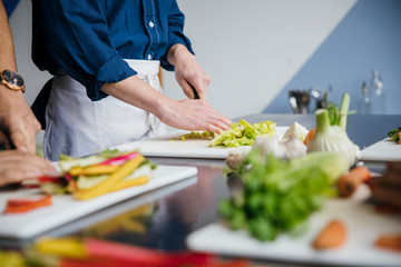 Midsection of male students chopping vegetables on table in training class