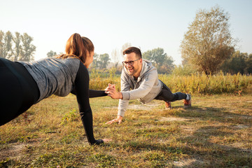 Happy fit young couple exercising by the lake or river in the early morning, holding hands while in plank position. Training abdominal muscles. Healthy and active lifestyle