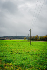 einzelne Stromtrasse mit Holzpfählen auf grünem Feld im Herbst