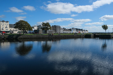 Fototapeta na wymiar Famous view of the brightly painted houses of Galway city and the River Corrib, with sail boats moored on calm water, with the sky reflecting in it. Taken on a sunny summer day.