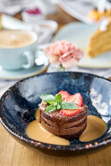 Chocolate sponge cake, with caramel, decorated with strawberries and mint leaf. Breakfast in the cafe, morning coffee. Cappuccino and lots of desserts on the table.