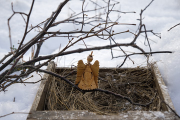 Christmas bark  angel in wood tray with dry grass and twig of  tree over white snow background.