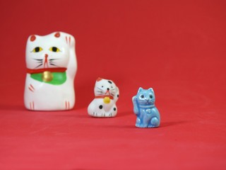 Three little Maneki Neko, Japanese lucky cats, amulets that bring good luck, protection, prosperity, health and happiness. The cat in the foreground is well focused. The others are out of focus.