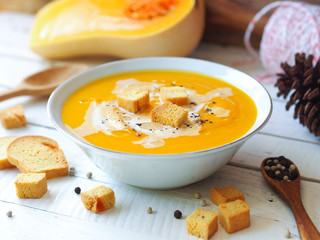Hot butternut squash pumpkin soup topping with fresh cream and crouton on a white rustic wooden...