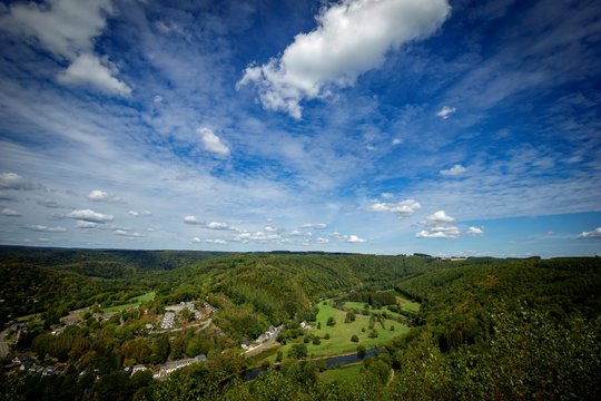 A landscape photograph of the area of Lafor&ecirc;t in the ardennes in Belgium with a blue sky and lots of forest. There is a village and the Semois river flowing through the woods.