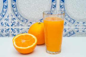 Glass of fresh orange juice and two oranges on the light ornamental background. Healthy food.