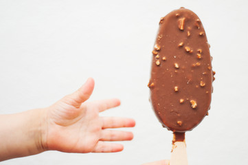 Small baby's hand reaching for the ice cream on a stick. Chocolate ice cream with nuts on white background..