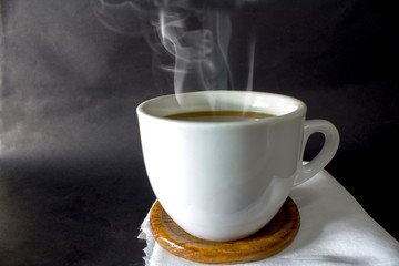 close up of a white coffee cup with hot smoke resting on a white cloth on a black background