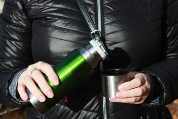 Woman pours tea from a thermos in the woods