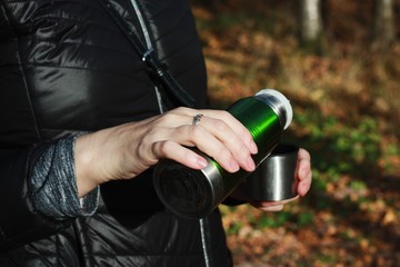 Naklejka premium Woman pours tea from a thermos in the woods