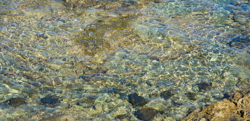 clear sea water with sun glare over the stone bottom