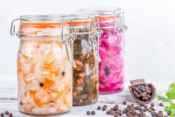 Fermented preserved vegetarian food. Homemade marinated cabbage kimchi, sea kale with carrot, sauerkraut sour in glass jars on rustic wooden kitchen table. Canned vegetables food concept