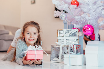Smiling child lying under fir-tree with a gift wrapped for Christmas.