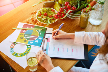 Woman dietitian in medical uniform with tape measure working on a diet plan sitting with different...