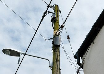 Old wooden telegraph pole seen next to a cottage showing a standard warning sign and both power and...
