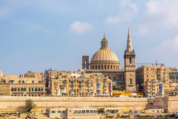 Fototapeta na wymiar Coastal landscape of Valletta at sunny summer day, with its traditional architecture of yellow limestone. Maltese Valletta skyline with church of Our Lady of Mount Carmel and St Paul's Pro-Cathedral.