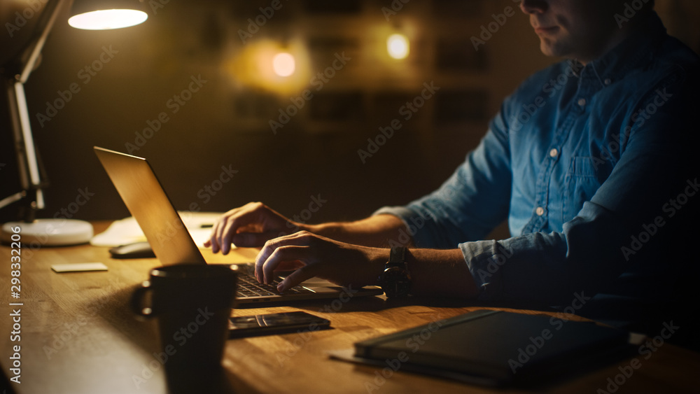 Aufkleber Anonymous Man Sitting at His Desk in Office Studio Working on a Laptop in the Evening. Man working with Data, Analyzing Statistics. 