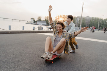 Cheerful son riding his mother on a skateboard and laughing. Single mother spending time with her...