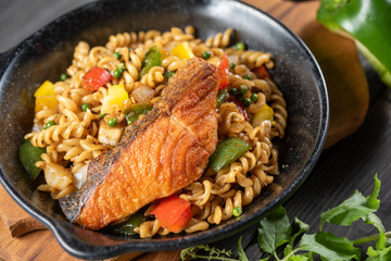 Spiral pasta fried 3 colors of bell pepper with fried salmon served on a black plate. Ingredients have salmon, onion, bell pepper and black pepper spicy and smell. Good food for good health