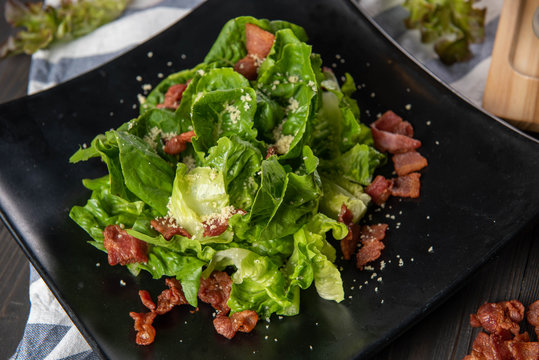 Caesar salad topped with crispy bacon and cheese Is beautiful arranged in a matt black plate. Fresh green vegetables have many vitamins for eat with main course dishes to receive complete nutrition