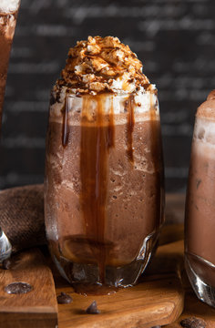 Ice chocolate, toppings by floating foam milk and Choco lava in a tall of clear glass on dark gray real wood and chopping board. Decorated with choc chip. Popular drink to quench thirst to cool down