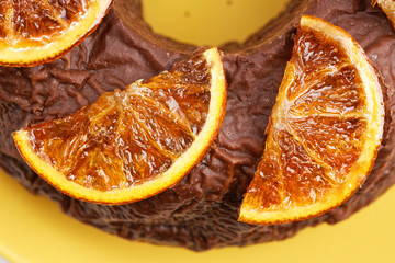 Closeup homemade chocolate cake decorated with candied orange slices on yellow plate. Top view.