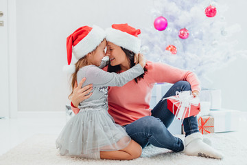 Obraz premium Caucasian mum and daughter are exchanging gifts on Christmas Eve. They are hugging one another and touching with noses.