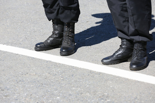 Legs of soldiers in black boots on the street. They stand along the white line.