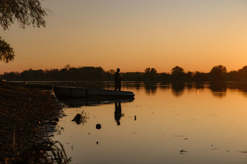 Silhouette of a fisherman. A man catches a fish by the river at sunset.