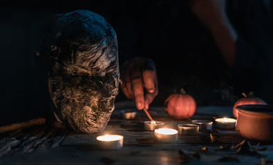 Witch doing curse and ceremony in the dark of Halloween night on the table with candles, skull and wand. Picture is partly focused and decorated in dark tone.