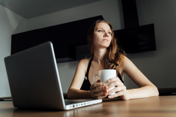 Young beautiful sad girl sits at a table in front of a laptop and dreams. Freelance, remote work