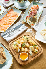 Cheese plate. Focus on delicious cheese mix with walnuts, honey on wooden table. Various snacks and antipasti on the table. Restaurant menu.