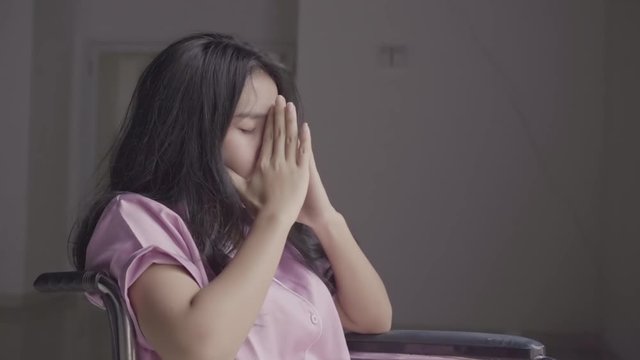 Depressed young woman sitting alone on wheelchair at home near the window