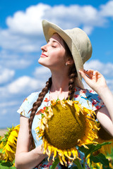 Young beautiful woman in a straw hat in a field of sunflowers