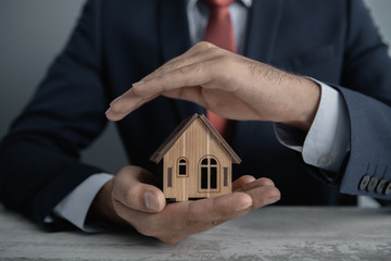 insurance; businessman holds a wooden house in his hands