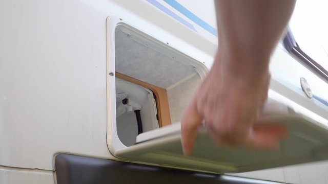 Slow motion close POV shot of a man&rsquo;s hand removing a chemical toilet waste disposal cassette from a caravan / motorhome / RV / camper, then closing the cupboard door.